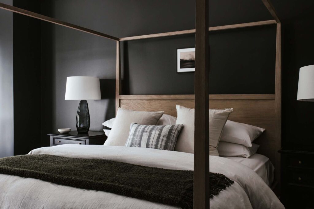 Primary bedroom with black walls and minimalist wood canopy bed