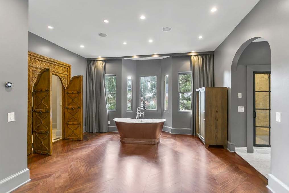 Before: primary bath in light gray with copper and white tub and rustic carved wood doors 