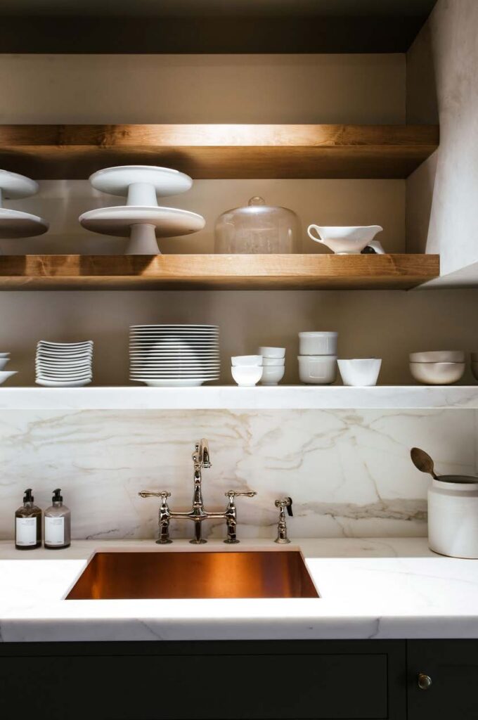 Copper sink with chrome fixtures and white marble counter and backsplash.